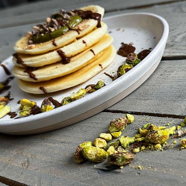 Fluffy Dubai-style protein pancakes topped with chocolate and pistachios, served on a white plate. A high-protein, healthy meal prep option.